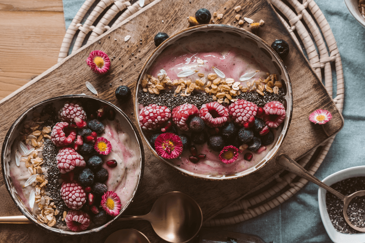 Zwei Schalen mit Joghurt, garniert mit Himbeeren, Heidelbeeren, Granatapfelkernen, Chiasamen und Haferflocken.