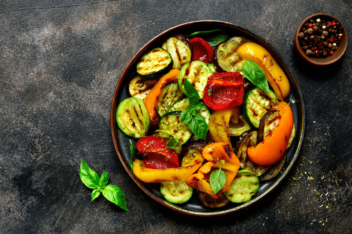 Gegrilltes Gemüse in einer Schale, darunter Zucchini, Paprika und Auberginen, garniert mit frischem Basilikum.