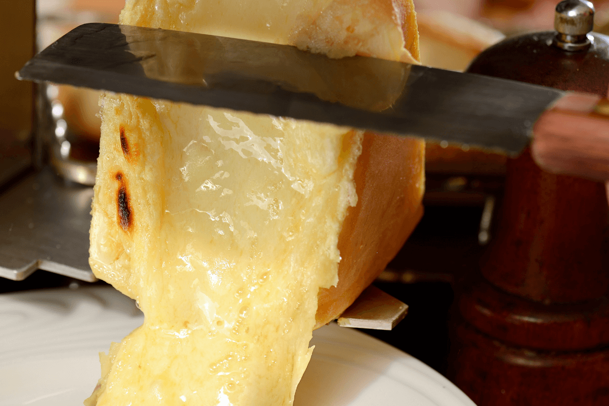 Raclettekäse wird mit einem Messer geschmolzen und über einen Teller gegossen, um eine köstliche Käseportion zu servieren.