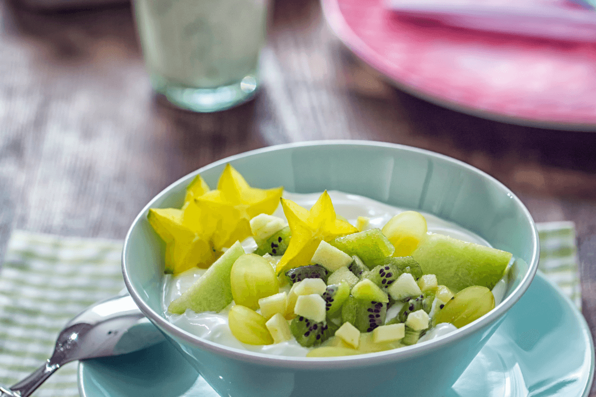 Schüssel mit Kiwi-Joghurt, garniert mit Sternfrucht, Trauben und grünem Apfelstücken. Frische und gesunde Zutaten.