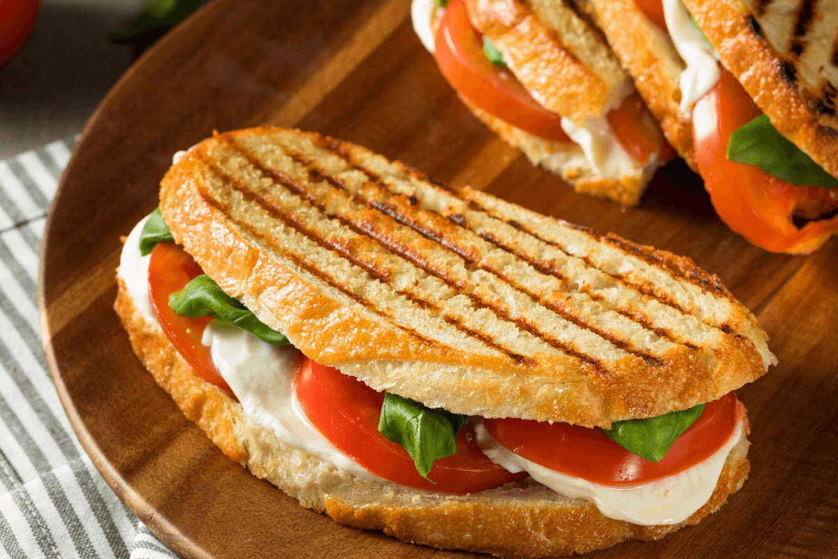 Panini mit Tomaten, Mozzarella und frischem Basilikum, perfekt geröstet mit Grillstreifen, auf einem Holzbrett.
