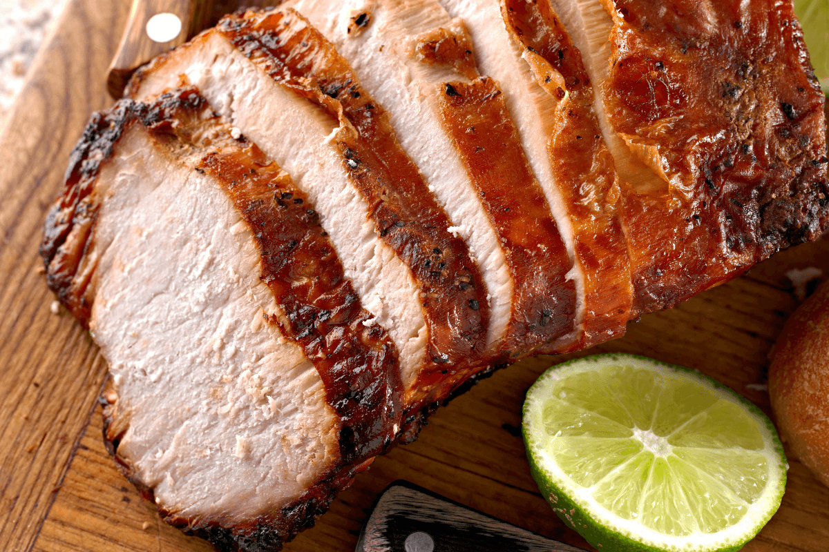 Saftig geschnittenes Fleisch auf einem Holzbrett, umgeben von Limettenscheiben und einem Küchenmesser.