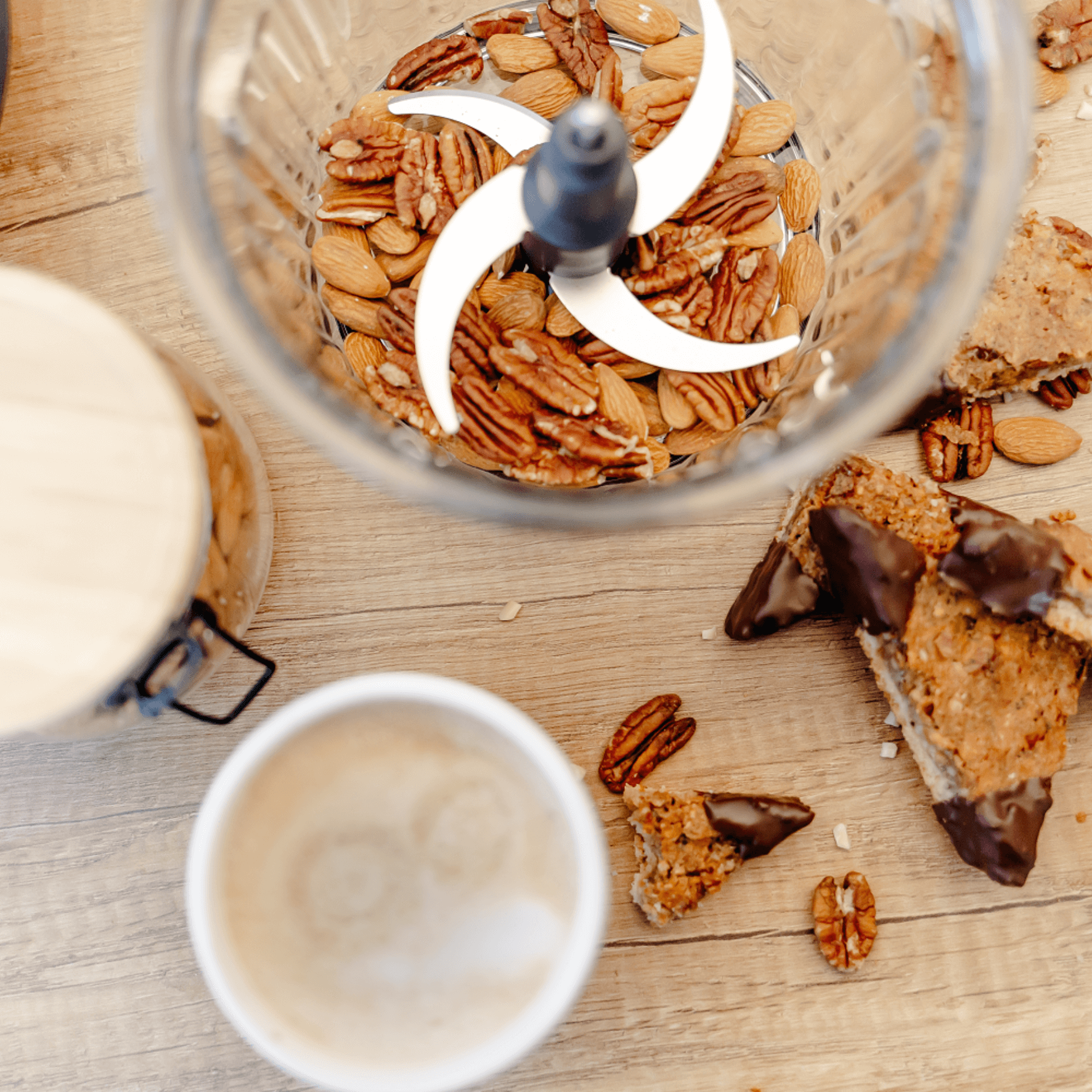 Eine Glas-Schüssel mit einem Messersatz, gefüllt mit Mandeln und Pekannüssen, umgeben von Snacks und einer Tasse Kaffee.