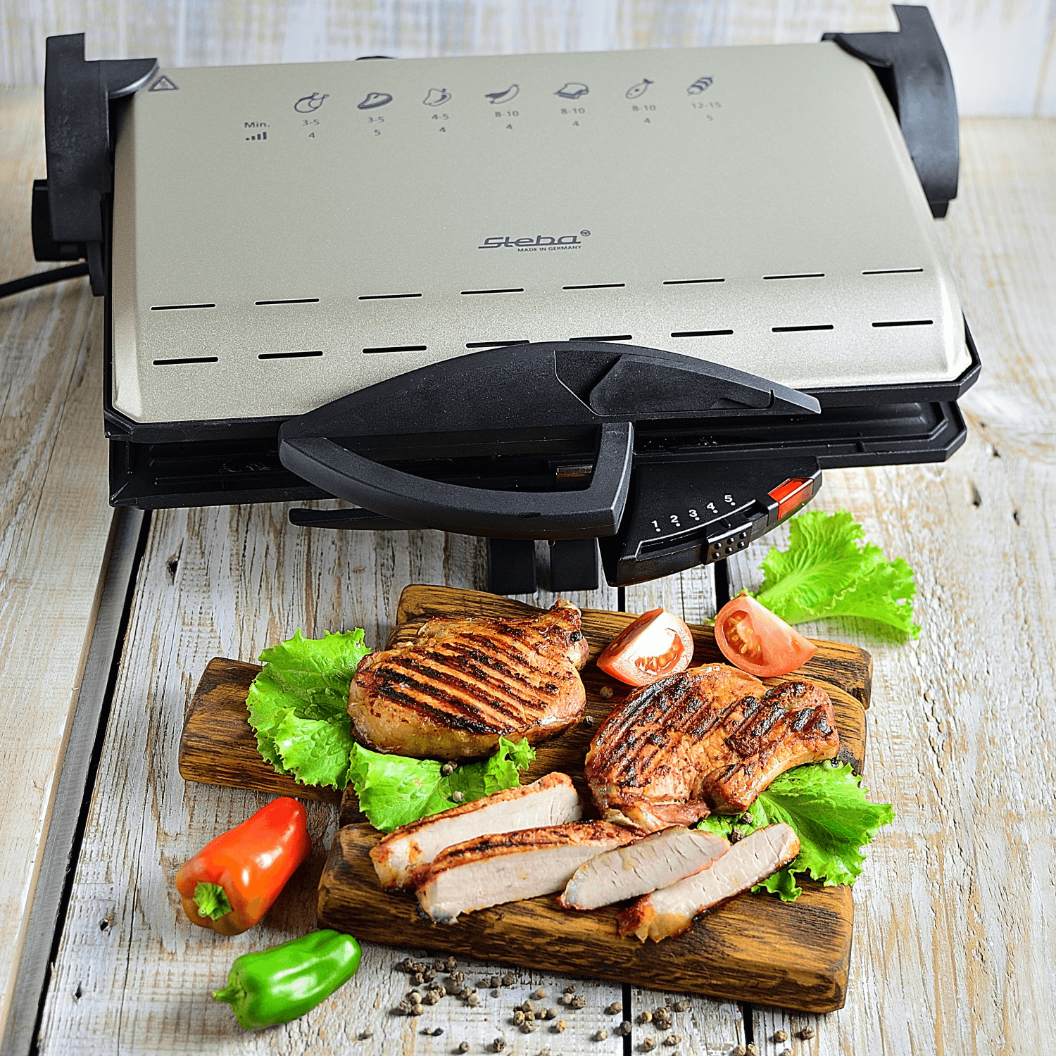Steba Kontaktgrill mit Grillfläche und Temperaturregler, daneben gegrilltes Fleisch auf einem Holzbrett mit Gemüse.