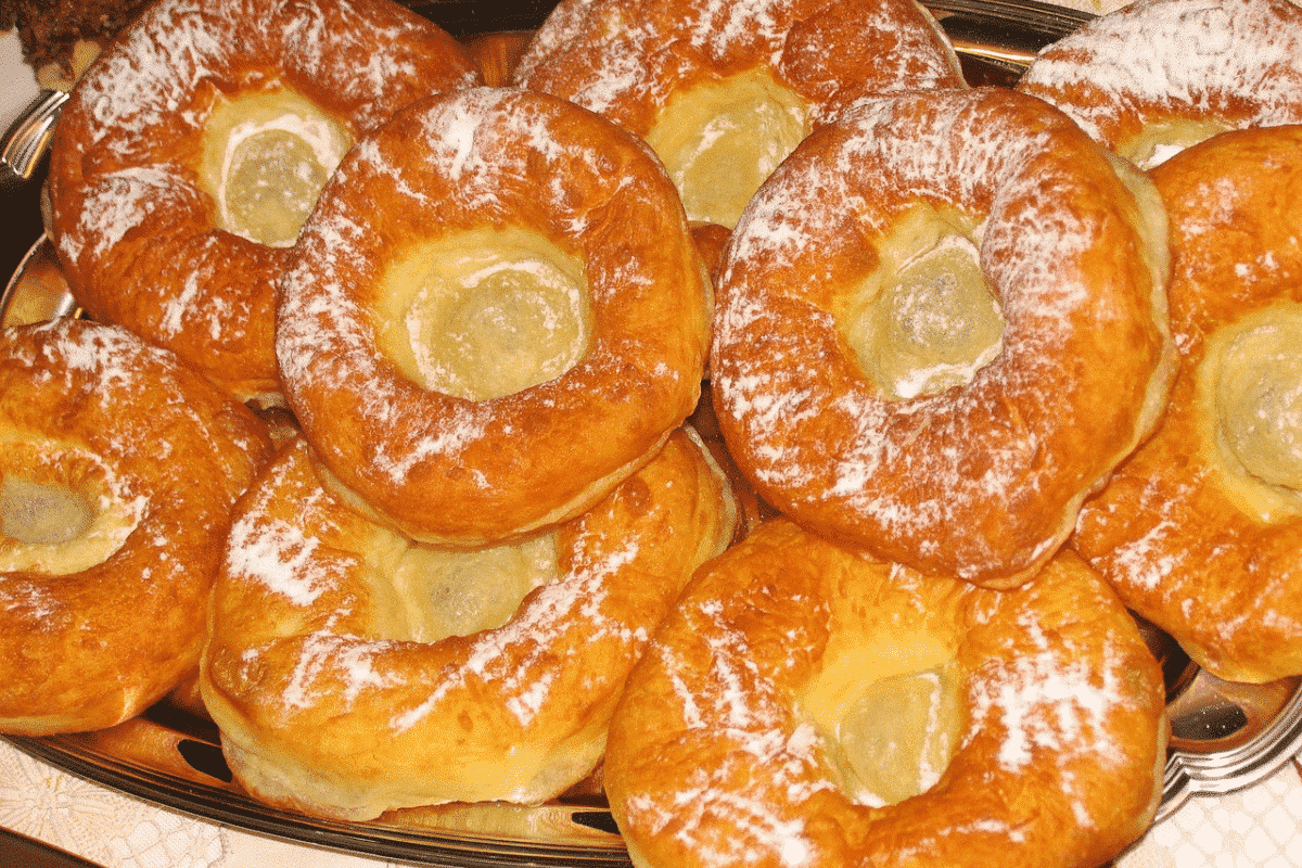 Ein Teller mit frisch gebackenen, leicht gefüllten Ausgezogenen Krapfen, goldbraun und mit Puderzucker bestäubt.