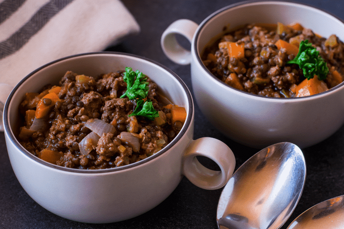 Zwei Schalen mit Hackfleisch-Gemüse-Eintopf, garniert mit frischer Petersilie, auf einem dunklen Tisch.
