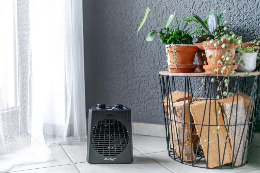 Luftheizlüfter von Steba in Schwarz, neben einem Pflanzenregal mit Töpfen und Holzscheiten. Ideal für angenehme Raumtemperatur.
