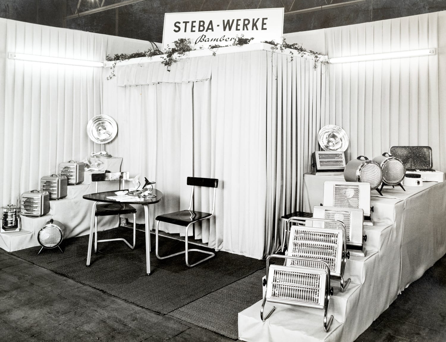 Messestand von Steba mit verschiedenen Elektrogeräten, darunter Heizgeräte und Küchenutensilien, in einem minimalistischen Design.