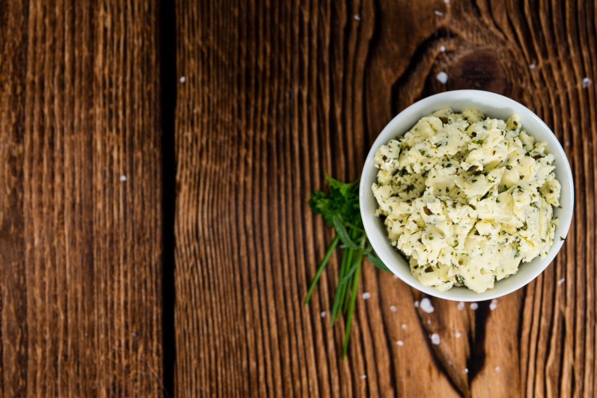 Schale mit Kräuterbutter, cremig und mit frischen Kräutern, auf einem rustikalen Holzuntergrund.