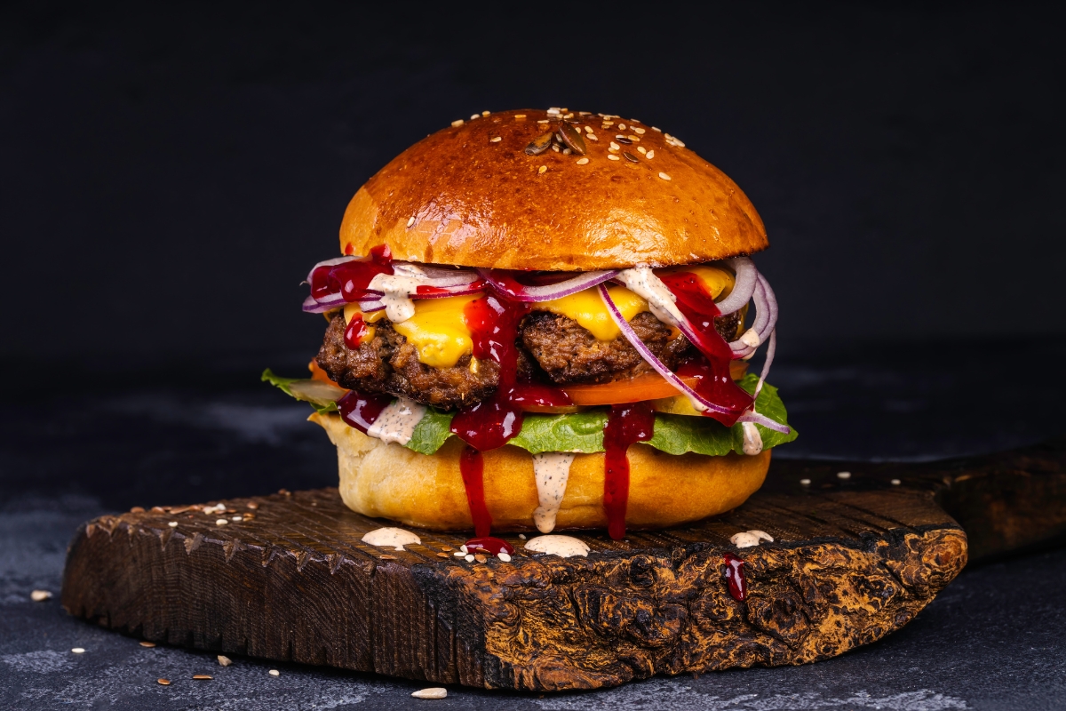 Saftiger Burger mit Käse, Zwiebeln, Salat und Saucen auf einem Holzbrett. Ideal für leckere Grillabende.