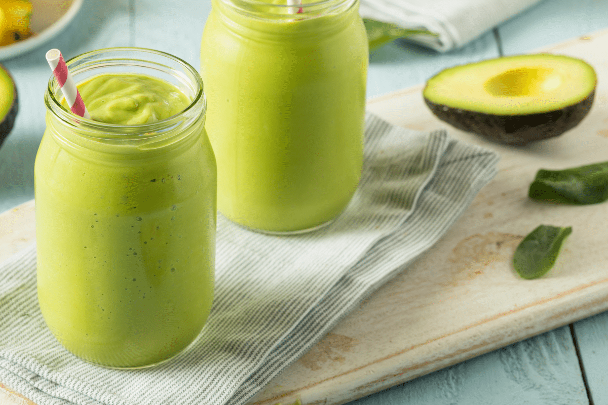 Zwei Gläser mit grünem Avocado-Smoothie, dekoriert mit einem Strohhalm, auf einem gestreiften Tuch.