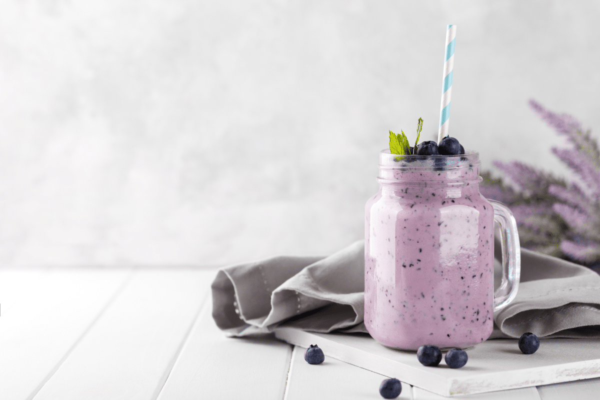 Ein Frühstücks-Smoothie in einem Glas mit einem Strohhalm, garniert mit Blaubeeren und Minze, auf einem Tisch.