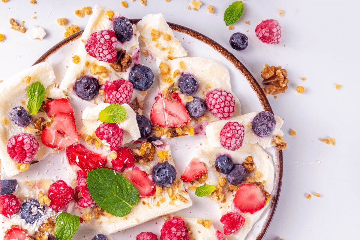 Ein Teller mit Frozen Yoghurt Häppchen, dekoriert mit frischen Beeren, Granola und Minzblättern.