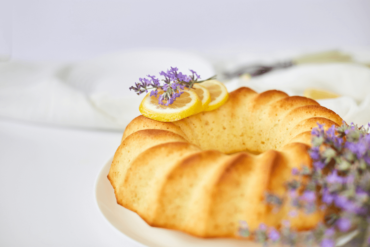 Saftiger Zitronenkuchen, dekoriert mit Zitronenscheiben und Lavendel, auf einem weißen Teller präsentiert.