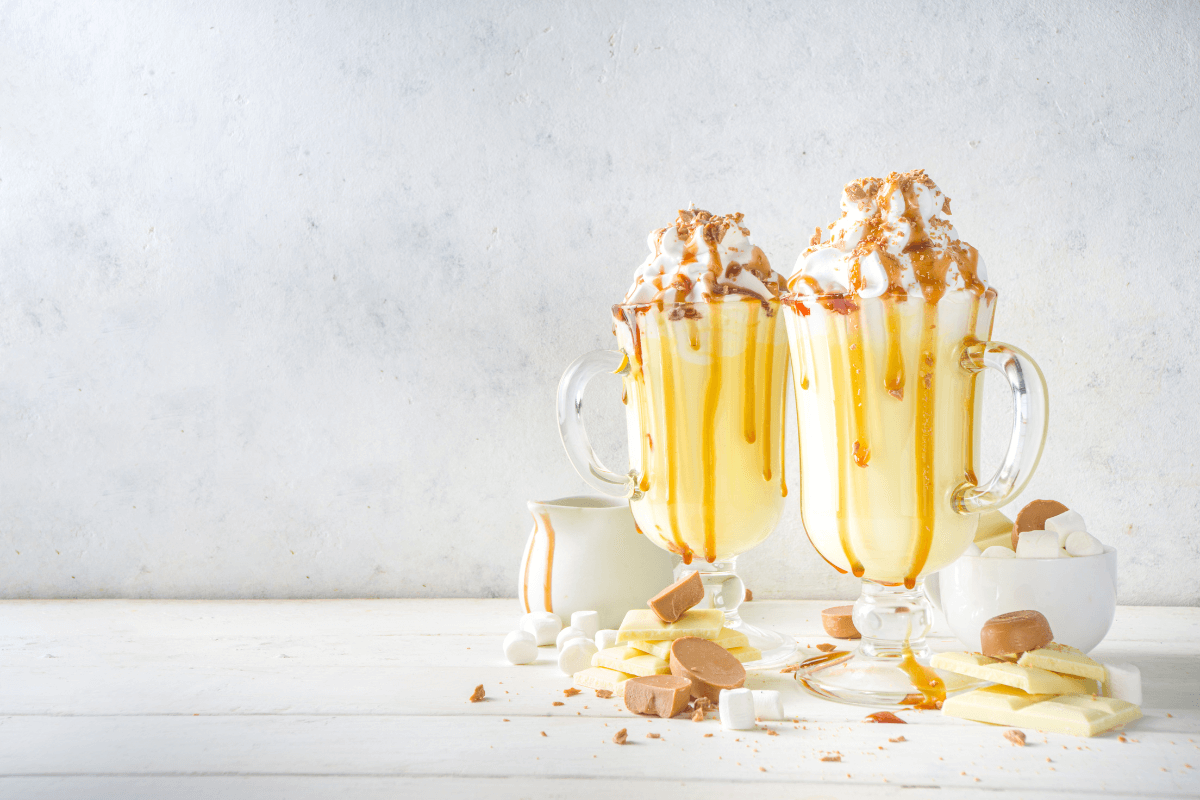 Zwei Gläser mit Eierlikör, dekoriert mit Sahne, Karamellsoße und Schokolade, umgeben von Süßigkeiten und Marshmallows.