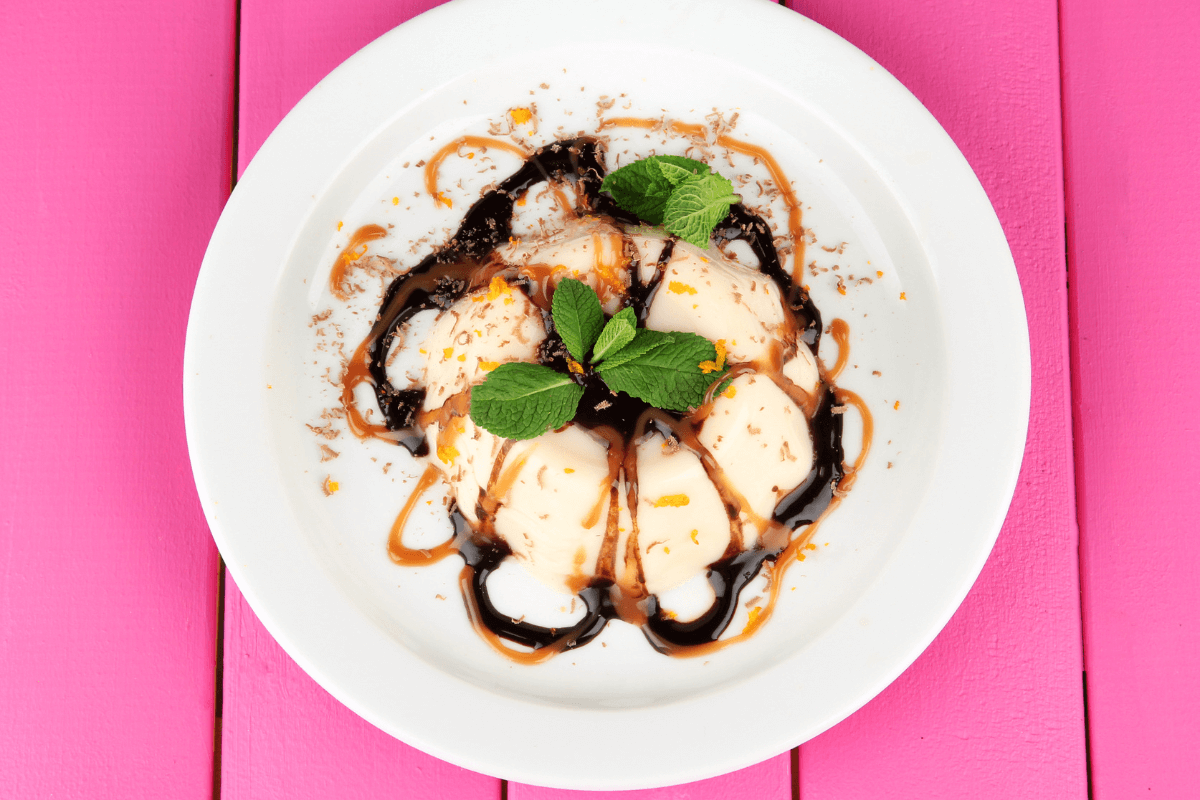 Panna Cotta mit Schokoladensauce, Karamell, Minze und Schokoladenspänen auf einem weißen Teller.