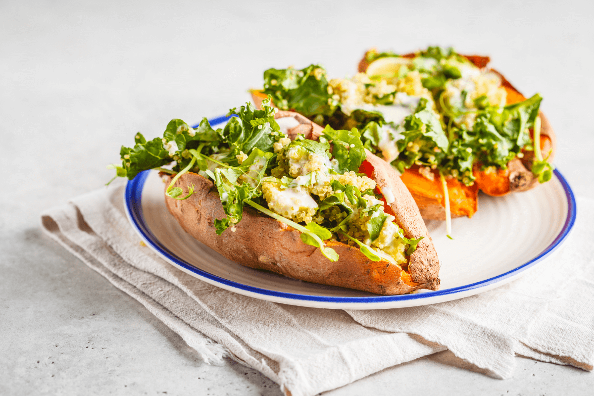 Gefüllte Süßkartoffeln mit Quinoa, Avocado und frischem Salat auf einem Teller, serviert auf einem hellen Tisch.