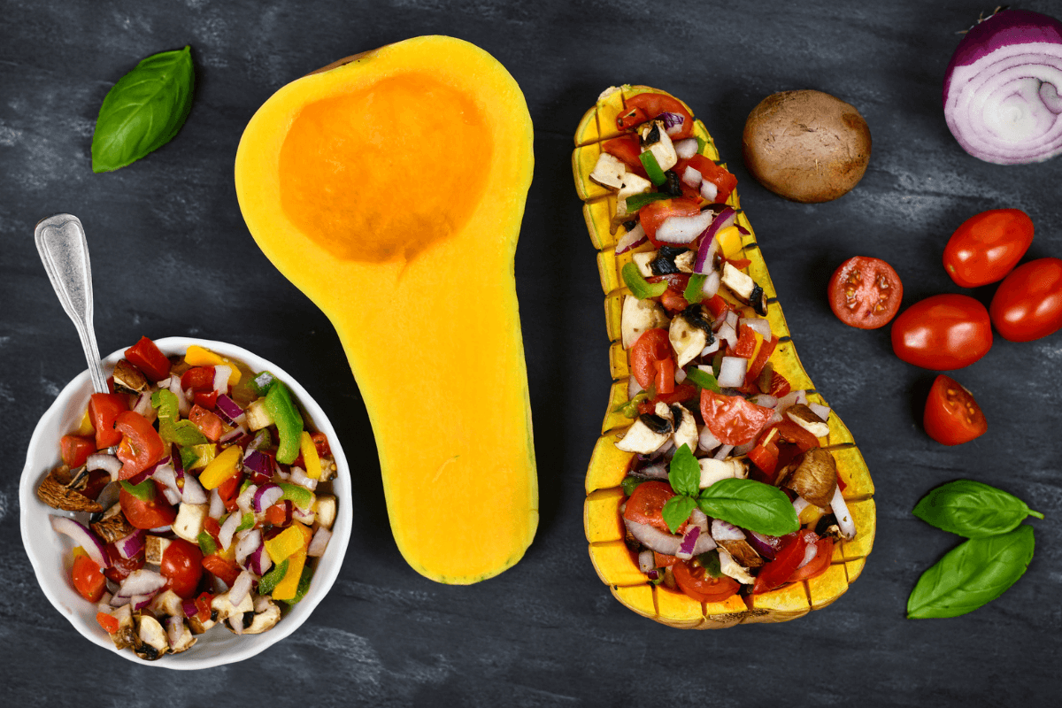 Gebackener Butternut-Kürbis, gefüllt mit Gemüse und Kräutern, neben einer Schüssel mit buntem Gemüsesalat.
