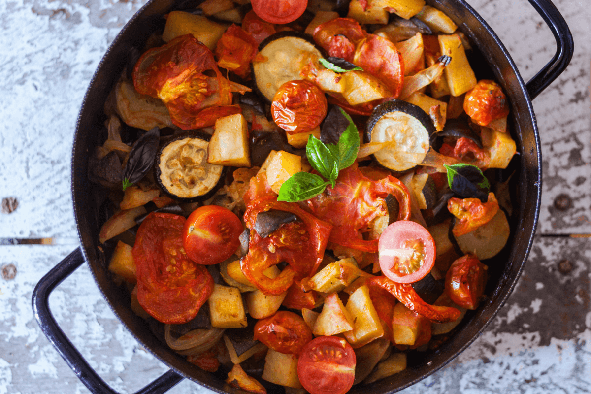 Mediterrane Gemüsepfanne mit Tomaten, Zucchini und Auberginen in einem schwarzen Topf, garniert mit frischem Basilikum.