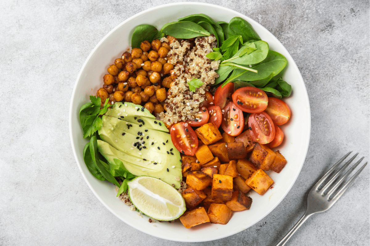 Bunte Quinoa-Bowl mit geröstetem Gemüse, Kichererbsen, Avocado, Cherrytomaten und Limette, serviert in einer weißen Schüssel.