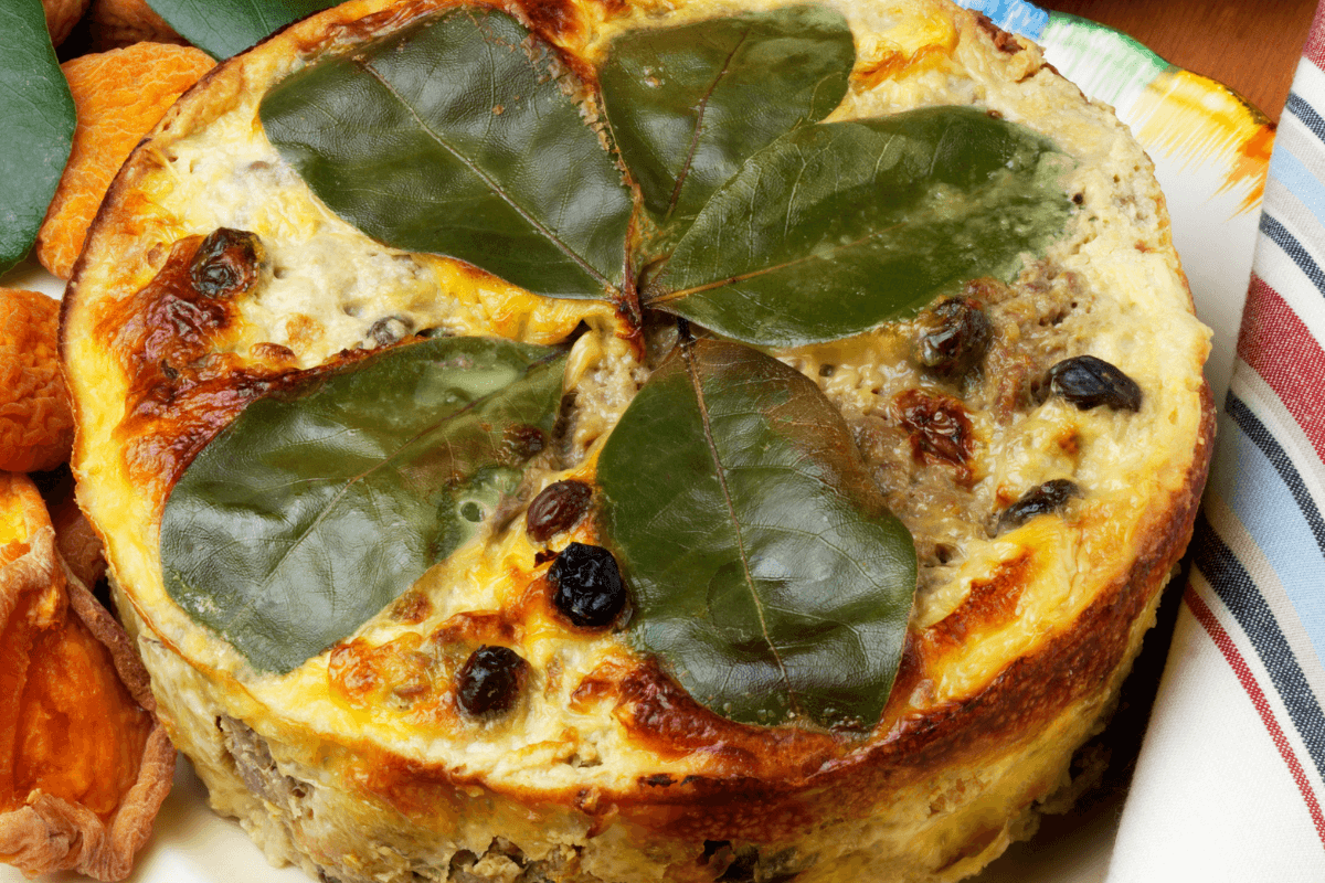 Ein gebackenes Bobotie mit goldbrauner Oberfläche, dekoriert mit Lorbeerblättern, serviert mit getrockneten Aprikosen.