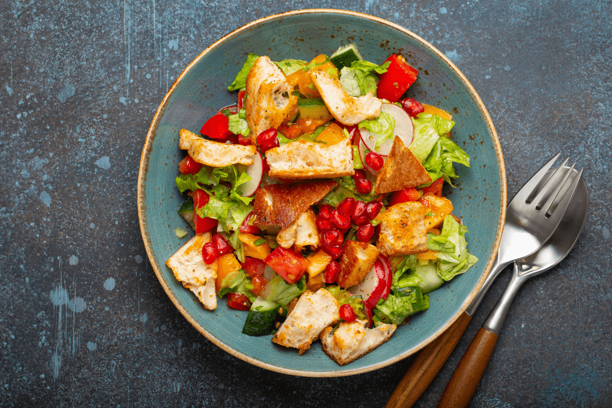 Bunte Fattoush-Salat-Schüssel mit Römersalat, Tomaten, Gurken, Paprika, Granatapfelkernen und geröstetem Brot.