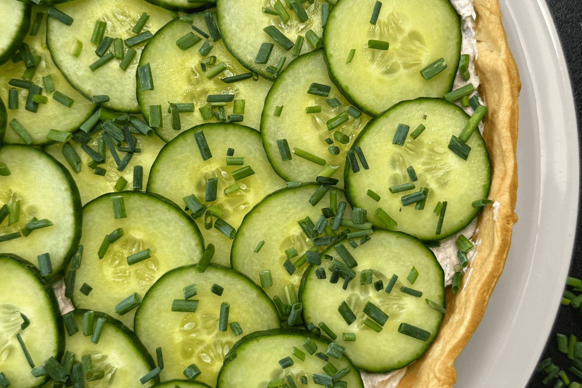 Schnelle Thunfisch-Tarte auf einem Teller, knuspriger Tarteboden mit cremiger Frischkäse-Thunfisch-Füllung, dekoriert mit Gurkenscheiben und frischem Schnittlauch.