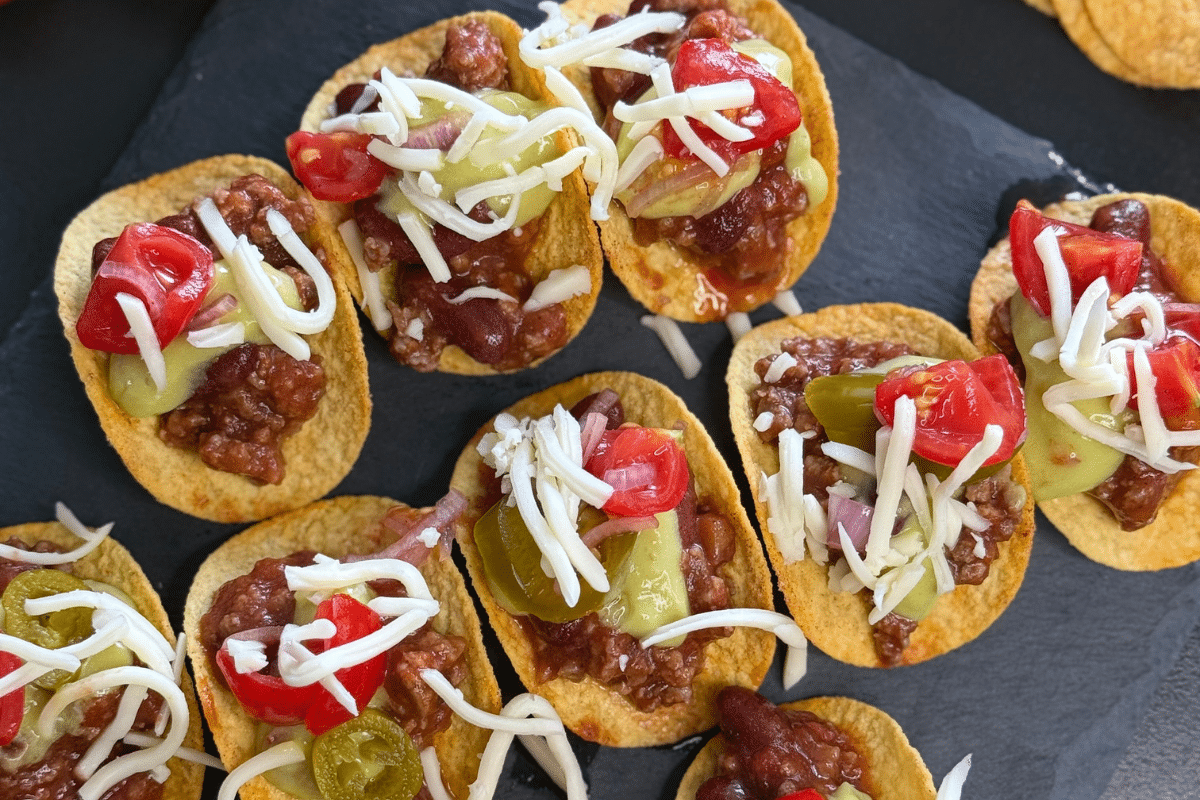 Pringles-Boote gefüllt mit Chili con Carne, belegt mit Käse, Tomaten, Jalapeños und Zwiebeln auf schwarzem Untergrund.