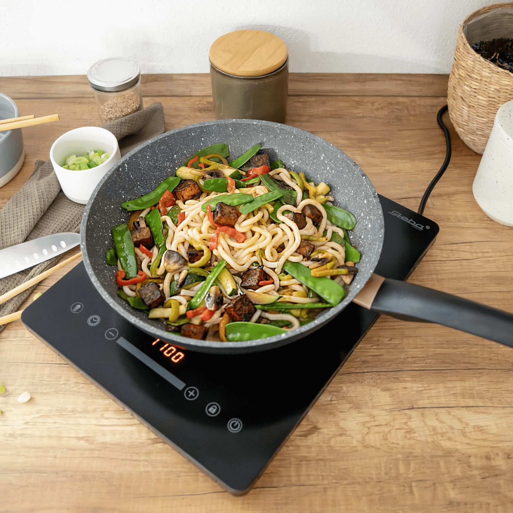 Pfanne mit buntem Gemüse und Nudeln auf einem Steba Induktionskochfeld. Digitale Temperaturanzeige bei 1100 W.